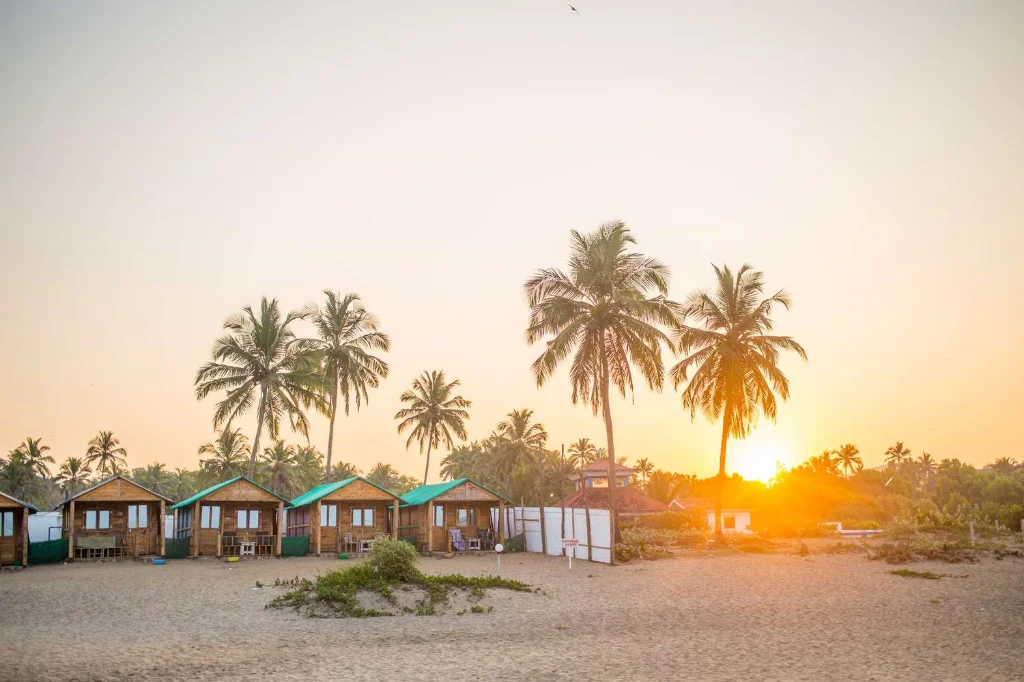 Elevated scenic view of Agonda Beach cove lined with shacks and coconut trees under a clear blue sky