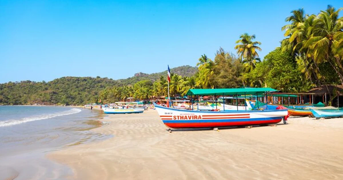 Colourful canopied boats lined up on the sand, with palm trees and green hills under a clear blue sky