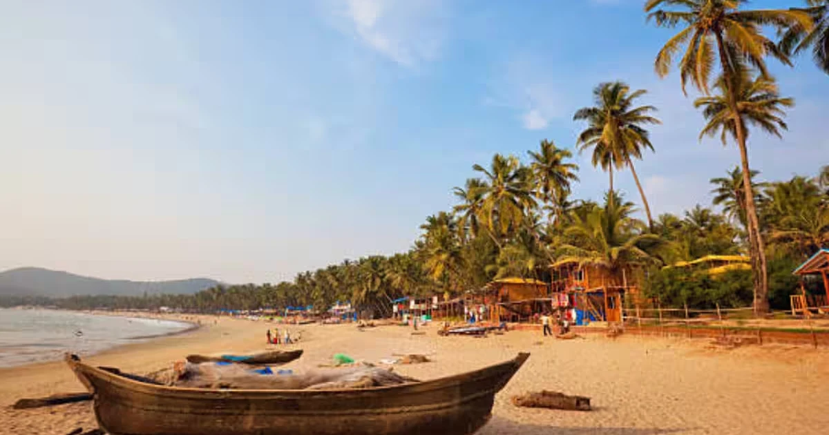 A wooden fishing boat resting on golden sand, with palm trees and beach huts lining the shore