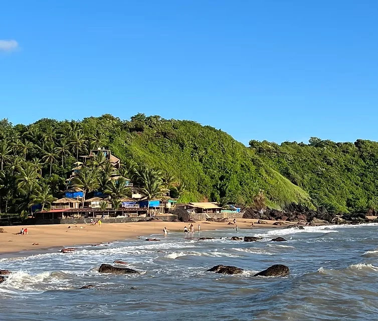 Waves crashing on volcanic rocks at the shoreline of Cola Beach with hill shacks in the background