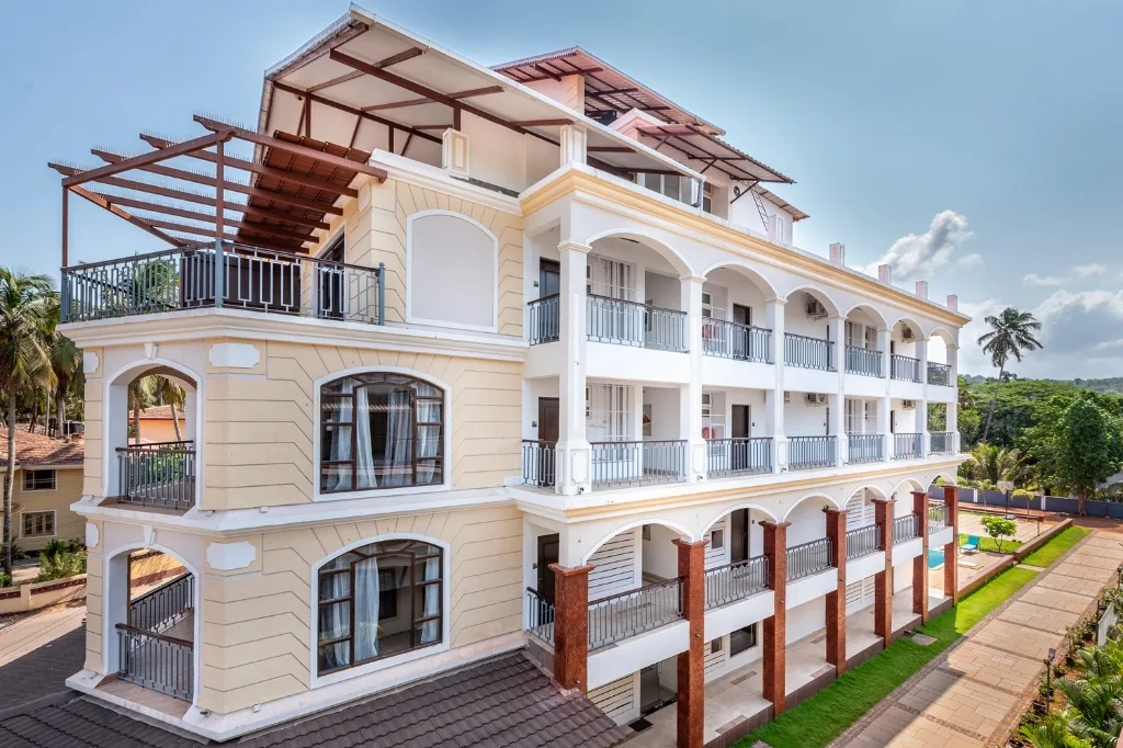 A multi-story luxury boutique hotel in Goa featuring white classical arches and balconies under a clear blue sky