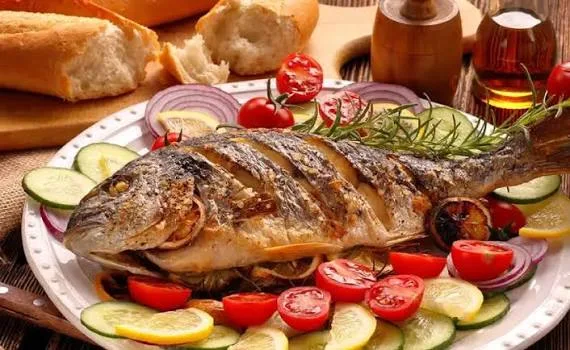 Whole baked fish served on a platter with cherry tomatoes, cucumbers, and lemons