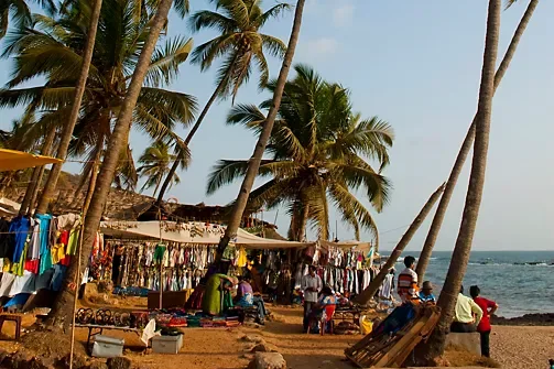 Beachfront market stalls under palm trees showcasing clothes, textiles, and local crafts near the shoreline