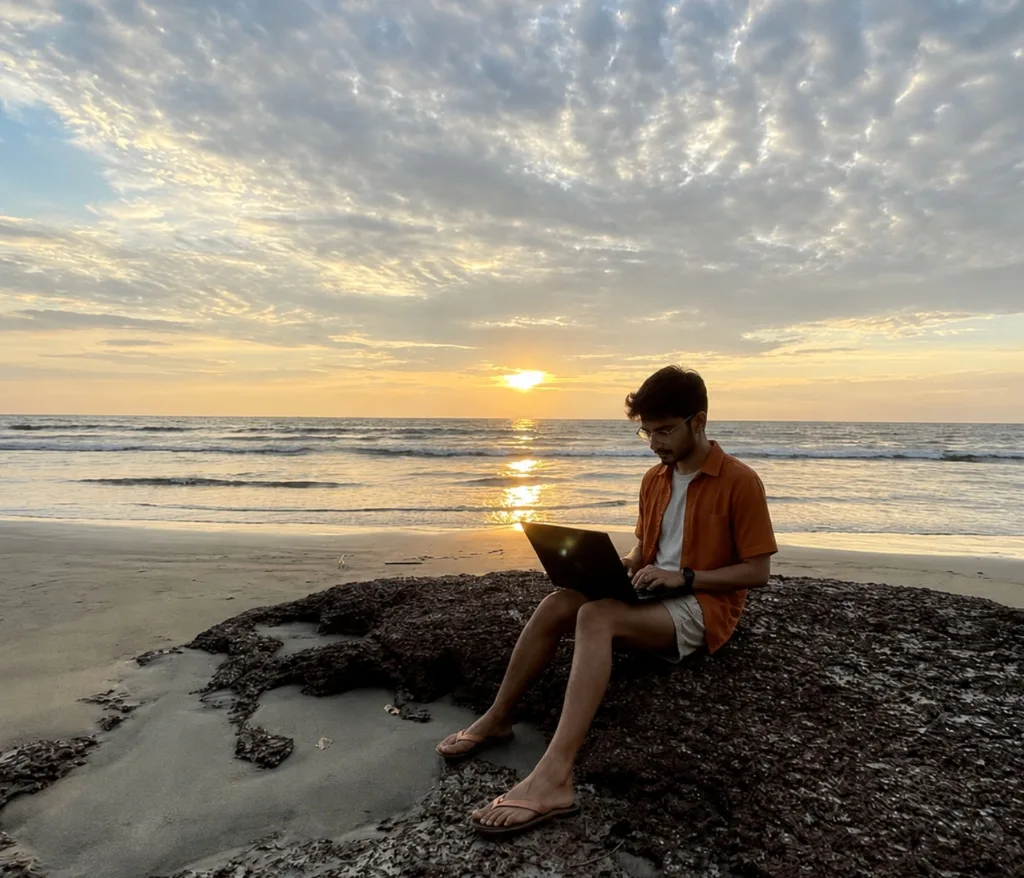 Remote worker sitting on a rock at sunset working on a laptop on Agonda Beach, South Goa