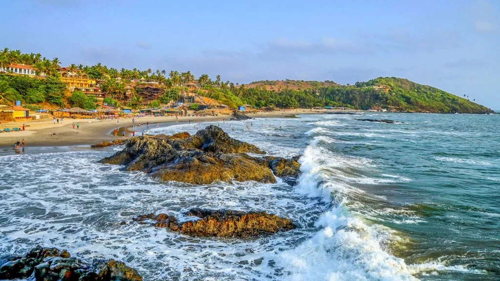 Beautiful landscape view of Vagator Beach, Goa, with dynamic waves crashing against rocky shoreline beneath a bright blue sky