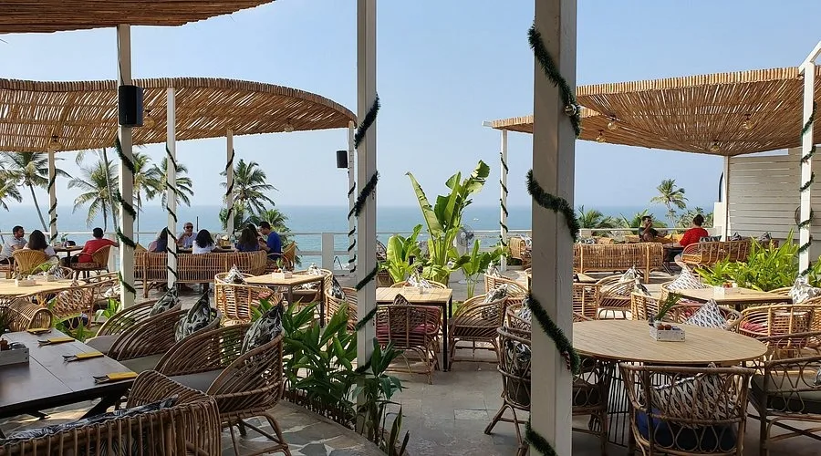 Spacious open-air cliffside restaurant in Vagator, Goa with cane chairs and tables looking out over the sea under bamboo thatched structures