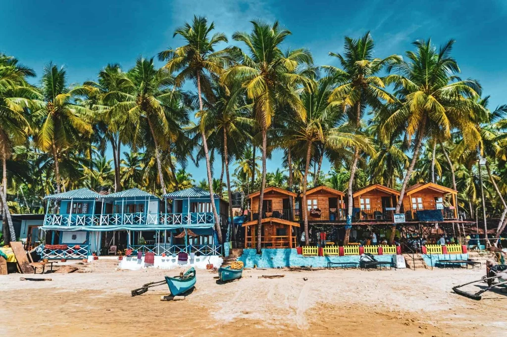 Colorful wooden beach huts under leaning coconut palm trees in Palolem Beach