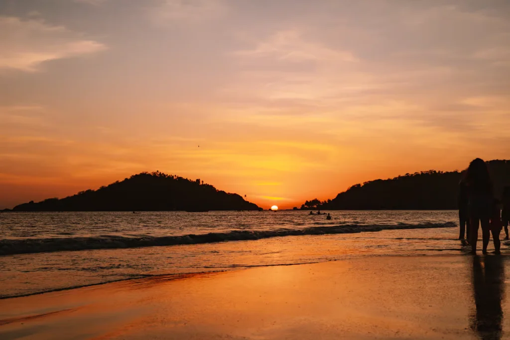 Spectacular golden sunset at Palolem Beach with silhouettes of islands and walking visitors